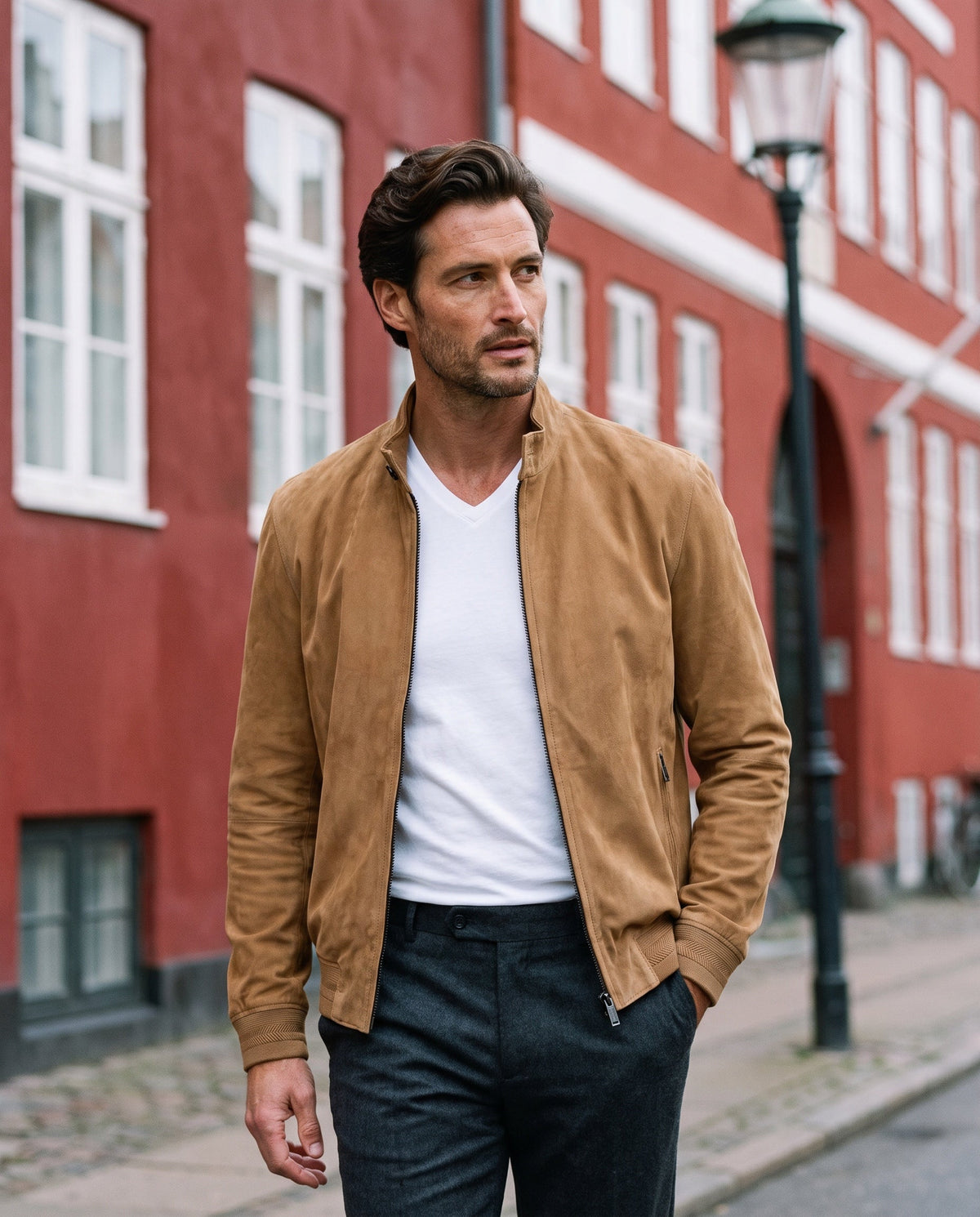 Model in a camel suede bomber jacket walking past a red facade in Copenhagen