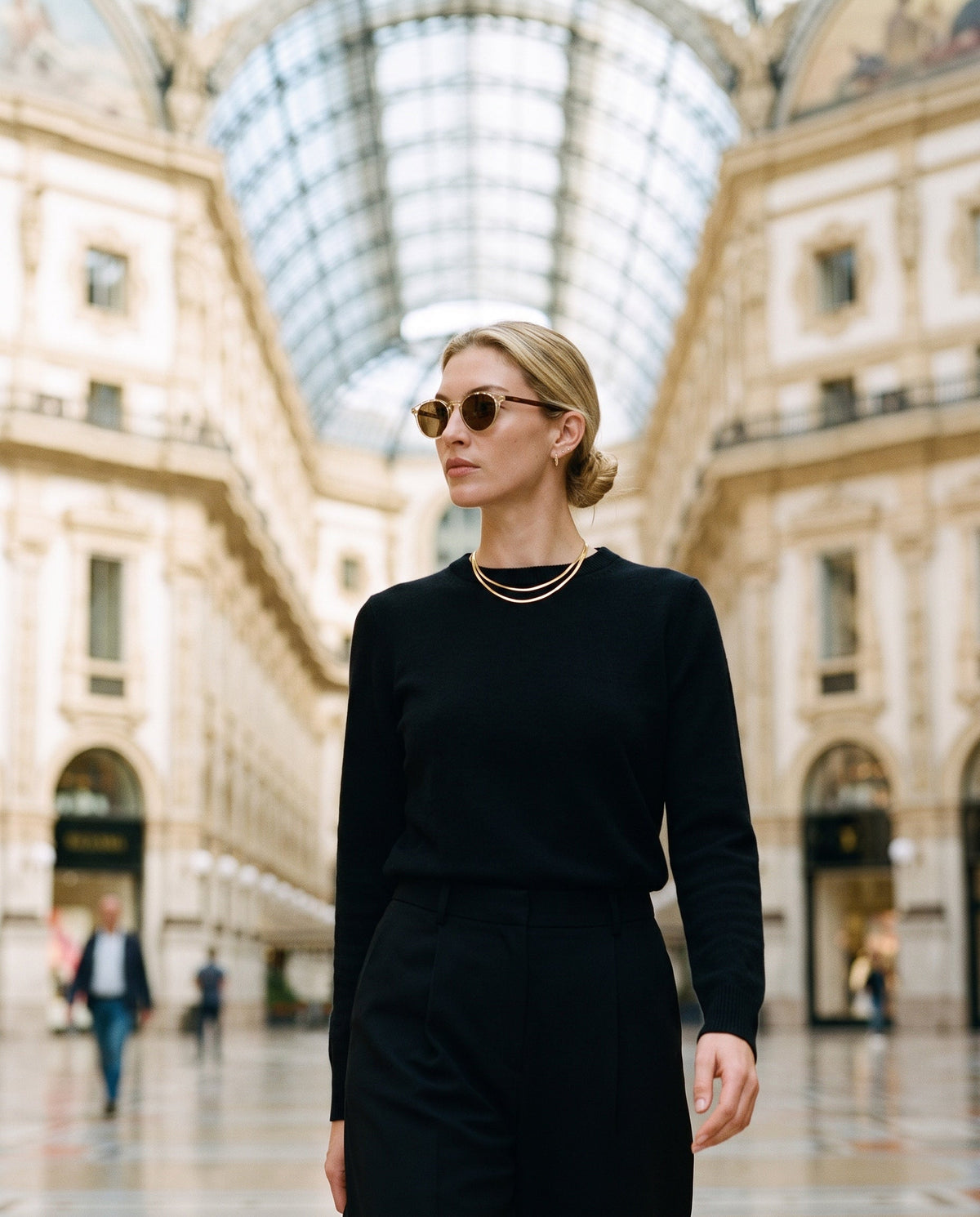 Model in a black knit, a gold choker and round tortoiseshell sunglasses in Milan's Galleria Vittorio Emanuele II