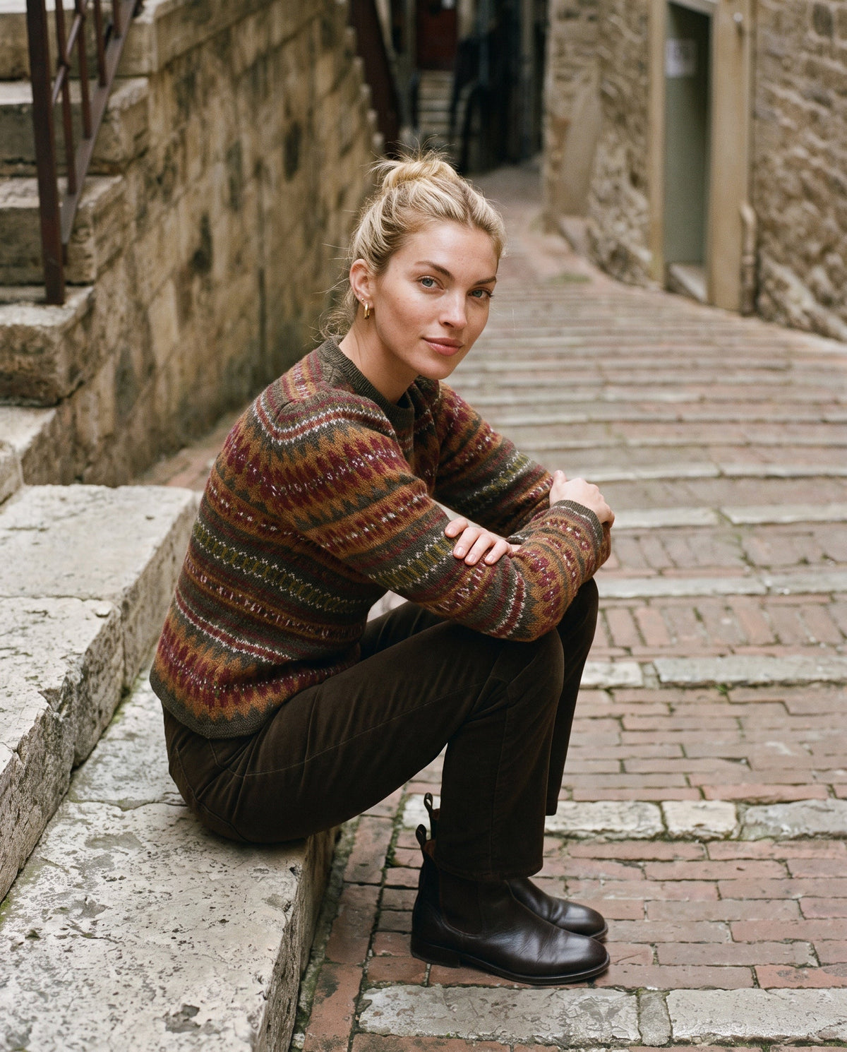Model in a jacquard wool and alpaca sweater sitting on stone steps in an alley in Perugia