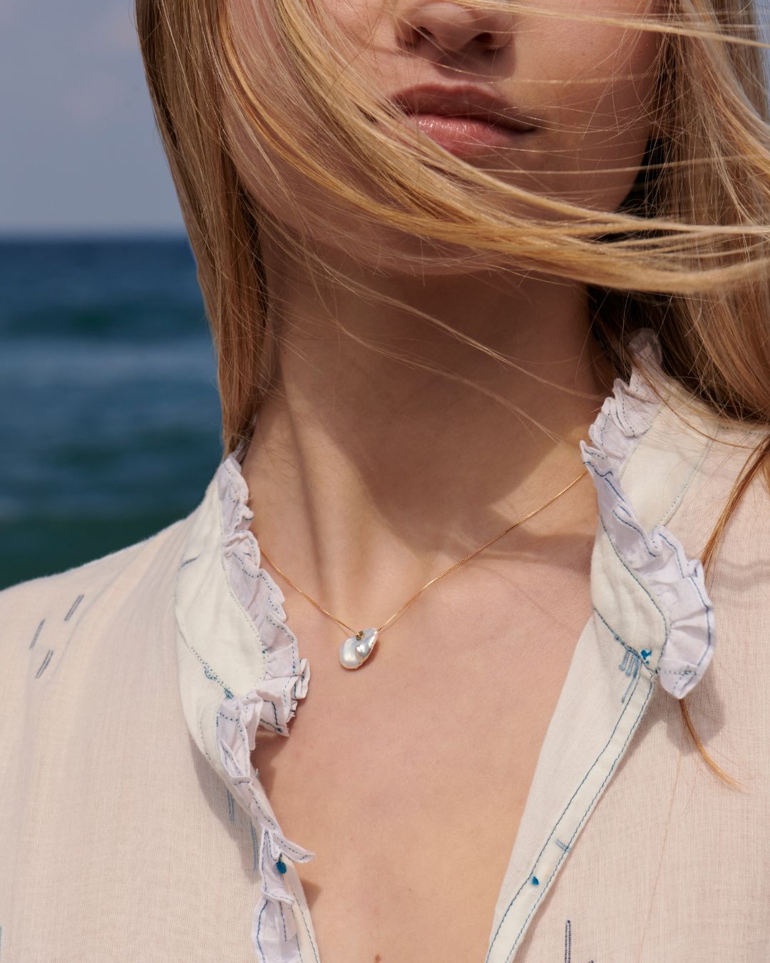 Atelier VM Brezza baroque pearl necklace worn at an open neckline by the sea