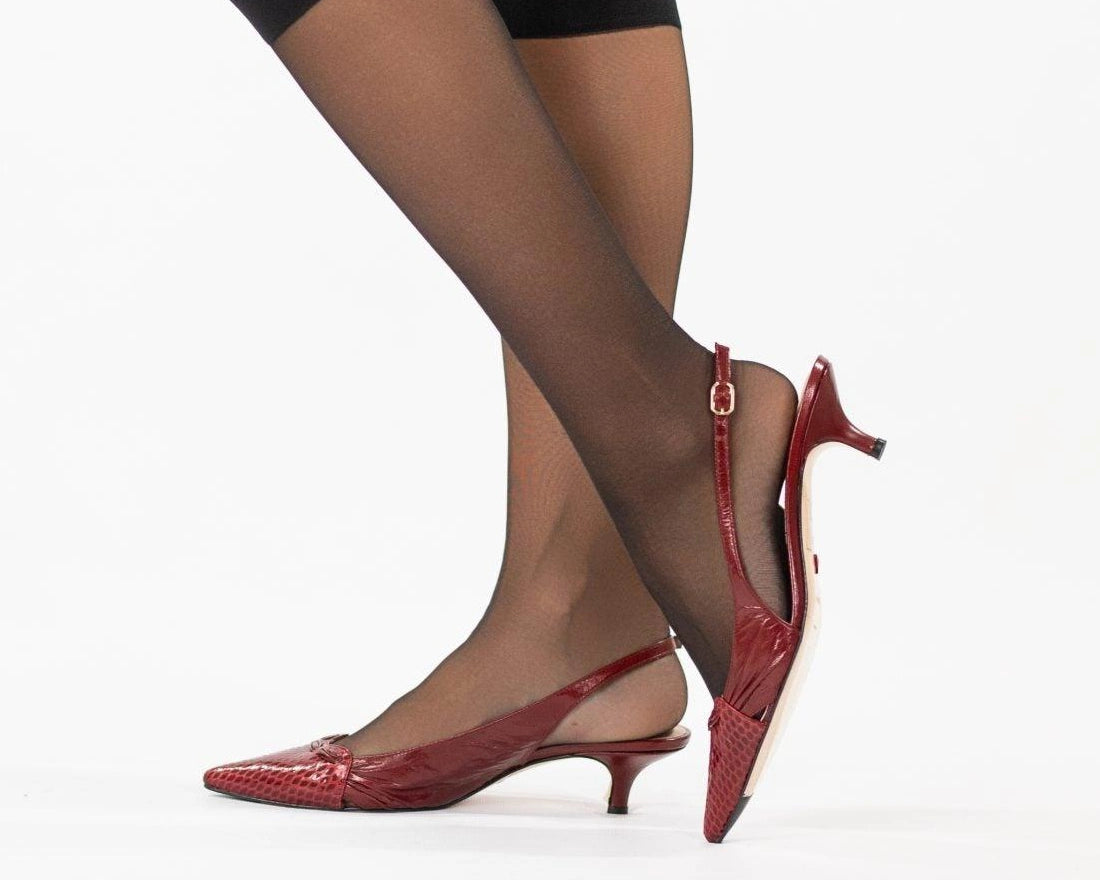 Magrit burgundy pointed slingbacks worn with sheer knee socks, one heel lifted